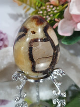 Load image into Gallery viewer, Septarian (Dragon Stone) Egg Crystal Carving Stone on Stand.
Grounds & Nurtures
Beautiful Polished Septarian Egg Crystal Carving on plastic stand. Has natural divits formations. Madagascar sourced.
Known as the Dragon Stone. Formed 70 million years ago from volcanic mud and sea life. These polished egg shaped feature cracked patterns of yellow Calcite, brown Aragonite and grey Limestone.The egg shape symbolises new beginnings, the "unfolding of energy from within,".