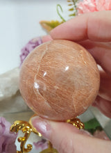Load image into Gallery viewer, Beautiful Peach Moonstone Sphere Crystal Carving on Gold Stand. Inspires balance and calms.