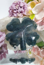 Load image into Gallery viewer, Beautiful polished Moss Agate Four Leaf Clover Crystal Carving on plastic stand. Insoires tranquility and grounding. 

HAS A SMALL CRACK on front and a lovely druzy on back
