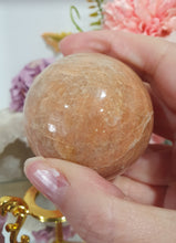 Load image into Gallery viewer, Beautiful Peach Moonstone Sphere Crystal Carving on Gold Stand. Inspires balance and calms.
